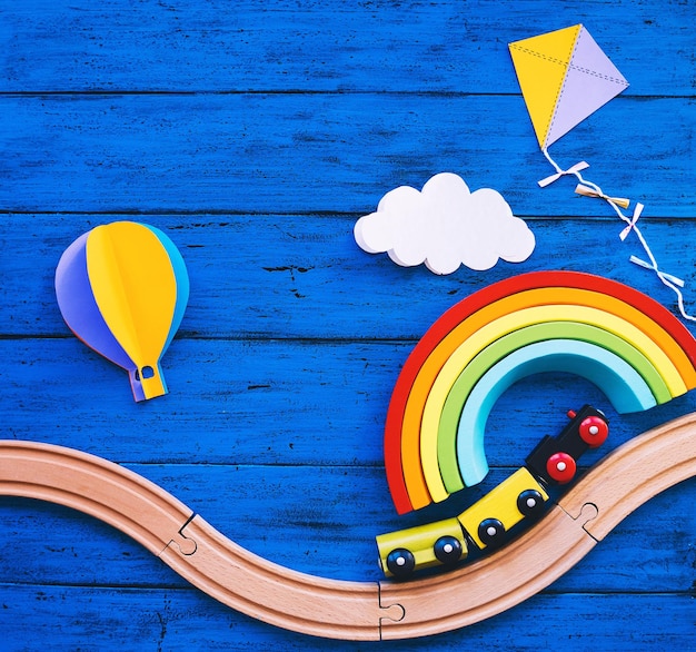 Ferrocarril de tren de juguete de madera para niños en edad preescolar manualidades de papel de arco iris de madera en la mesa azul Fondo de la escuela Waldorf o montessori Concepto de viaje de ensueño para niños Juguetes educativos para niños de jardín de infantes