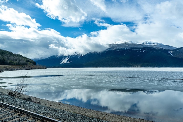 Ferrovia na margem do lago congelado Cordilheira sobre céu azul nuvens brancas Montanhas Rochosas canadenses