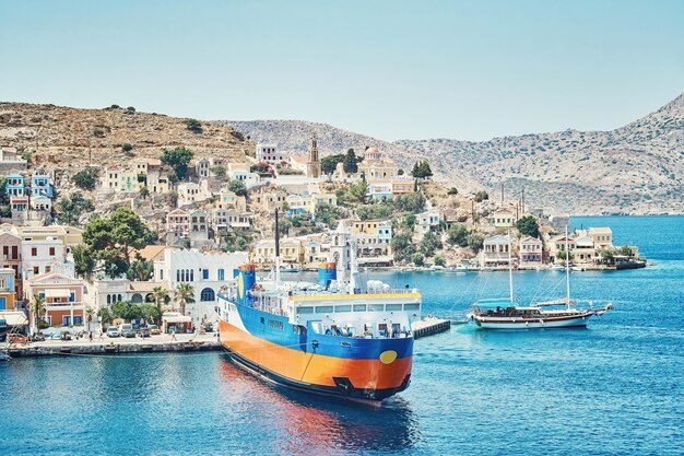 Ferry de crucero amarrado en el mar contra la ciudad con viejos edificios multicolores en las colinas de la isla de Symi