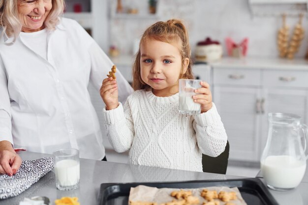 Fertig zum Essen Ältere Großmutter mit ihrer kleinen Enkelin kocht Süßigkeiten für Weihnachten in der Küche