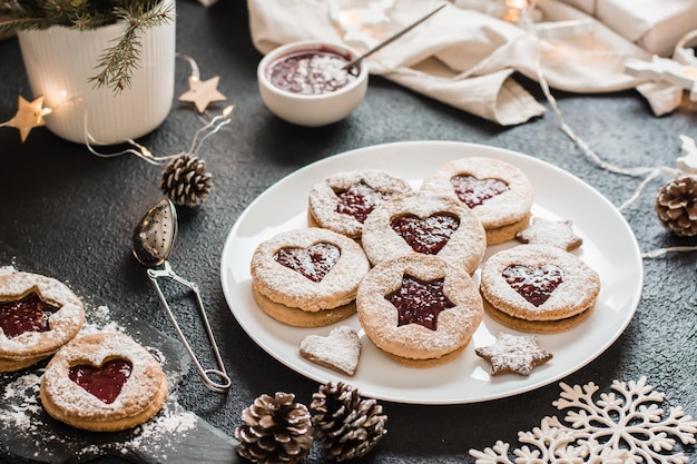 Fertige Linzer Kekse mit Beerenmarmelade auf einem Teller auf dunklem Hintergrund. Weihnachtsleckereien kochen. Lebensstil