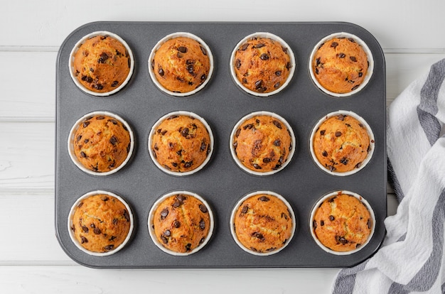 Fertige Muffins mit Schokoladenstückchen in Backform auf weißem Holzhintergrund. Rezept Schritt für Schritt. Ansicht von oben.