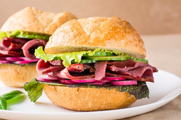 Fertiger Hamburger mit Pastrami, Gemüse und Basilikum auf einem Teller auf Kraftpapier. Amerikanisches Fastfood. Nahansicht