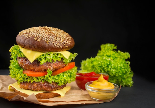 Fertiger Hamburger mit Rinderkoteletts, Käsegurke, frischen Tomaten und Salat auf dunklem Hintergrund Fast Food Cooking Copy Space Platz für Text