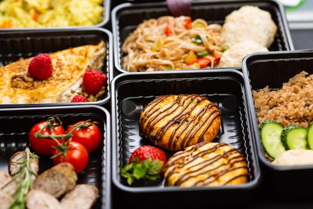 Fertiges Catering-Menü für gesunde Lebensmittel in Lunchboxen mit Fleisch- und Gemüsepaketen auf schwarzem Tischhintergrund