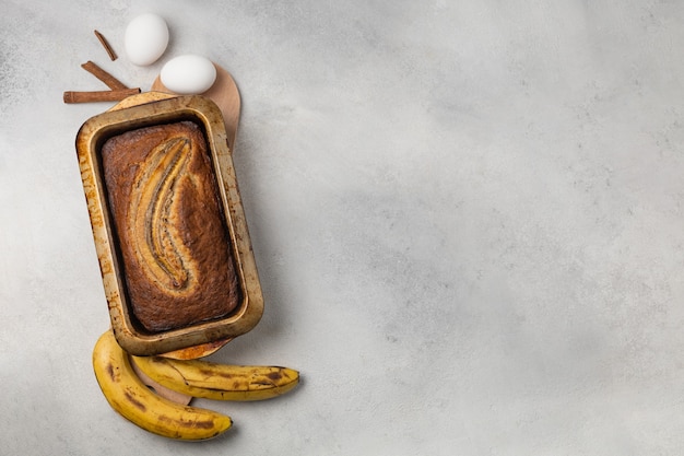 Fertiges frisches Bananenbrot in einer rechteckigen Auflaufform mit Zutaten auf hellem Hintergrund