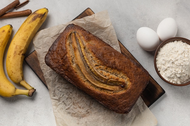 Fertiges frisches Bananenbrot in einer rechteckigen Auflaufform mit Zutaten auf hellem Hintergrund