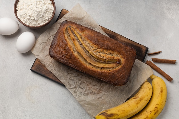 Fertiges frisches Bananenbrot in einer rechteckigen Auflaufform mit Zutaten auf hellem Hintergrund