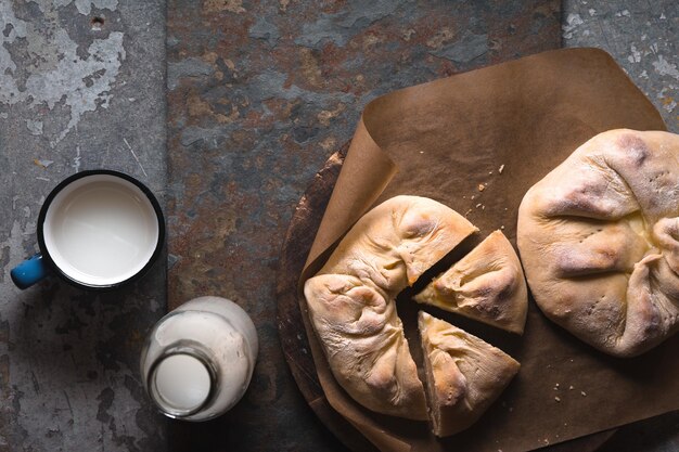 Fertiges Khachapuri mit Käse und Stücken auf Pergament und Milch in einer diagonalen Flasche