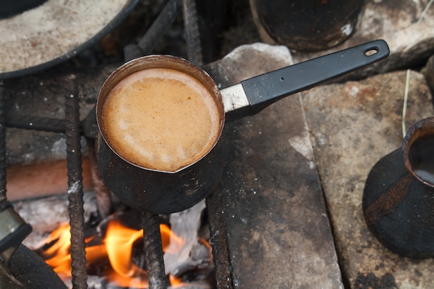 Fervendo café em cezva turco em uma grelha sobre uma fogueira ardente, um conceito de campismo