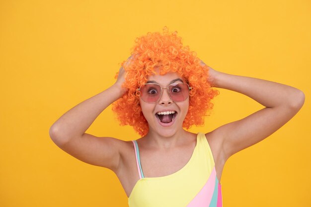 festa de aniversário. garoto engraçado na peruca de palhaço encaracolado. se divertindo. criança surpreendida usa óculos escuros e maiô. menina adolescente espantada com cabelo laranja. moda praia de verão. dia da mentira. Infância feliz.