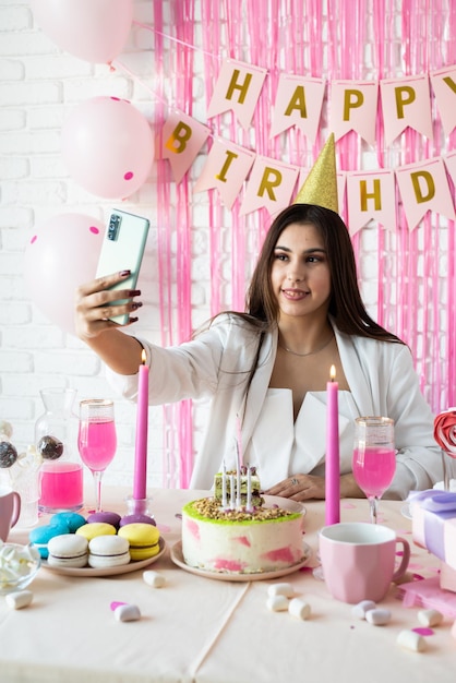 Festa de aniversário Mesas de aniversário Mulher atraente em roupas de festa branca comemorando aniversário tomando selfie no celular