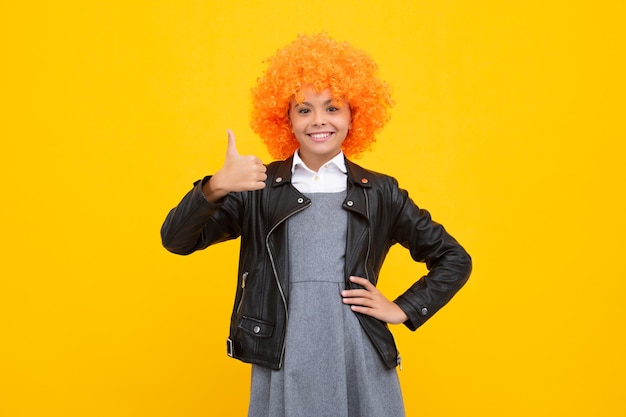 Festa de aniversário para crianças Criança engraçada com peruca de palhaço encaracolada isolada em fundo amarelo Garota feliz enfrenta emoções positivas e sorridentes