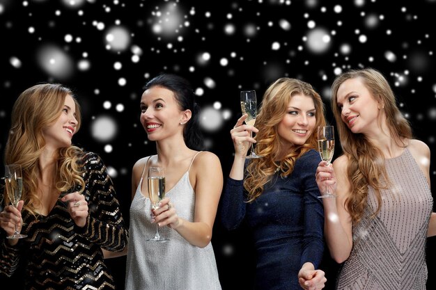 festa de ano novo, natal, férias de inverno e conceito de pessoas - mulheres felizes com taças de champanhe e dançando sobre fundo preto com neve
