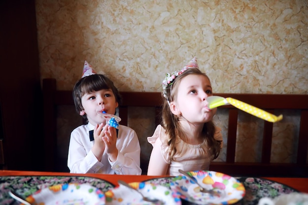 Festa de crianças em bonés comemorando aniversário com bolo e balões em casa.