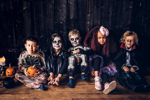 Festa de halloween com crianças do grupo que se sentam juntas em um piso de madeira em uma casa velha.