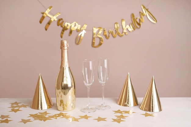 Festa dourada tampa uma garrafa de taças de champanhe e uma inscrição feliz aniversário na mesa Fundo festivo bege com espaço de cópia