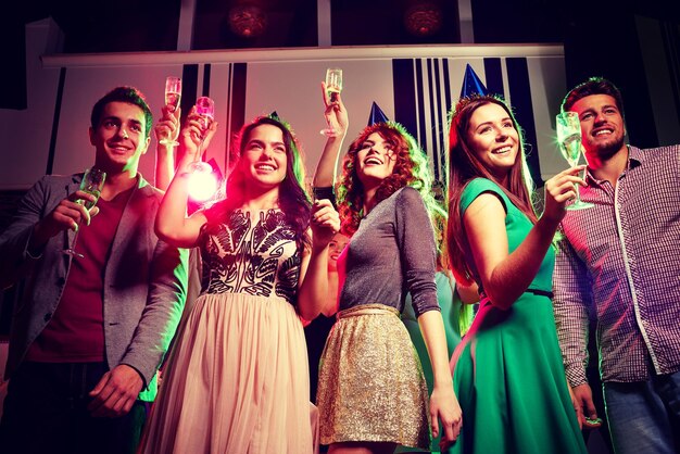 festa, feriados, celebração, vida noturna e conceito de pessoas - amigos sorridentes em bonés de festa com taças de champanhe no clube