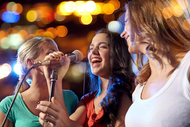 Foto festa, feriados, celebração, vida noturna e conceito de pessoas - mulheres jovens felizes cantando karaokê na boate