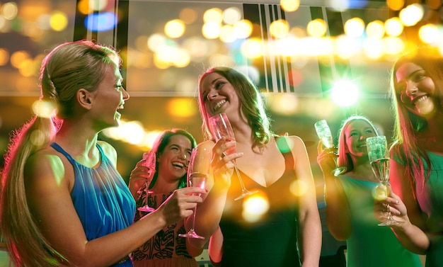 Festa, feriados, celebração, vida noturna e conceito de pessoas - mulheres jovens felizes com taças de champanhe no clube