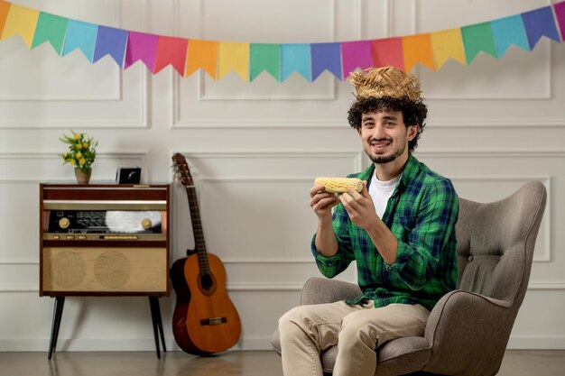 Festa junina bonitinho de chapéu de palha com rádio retrô e bandeiras coloridas comendo milho