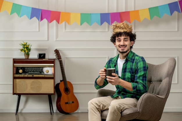 Festa junina bonitinho de chapéu de palha com rádio retrô e bandeiras coloridas segurando uma xícara de café