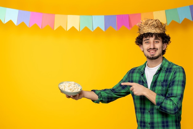 Festa junina chico lindo joven en sombrero de paja y banderas de colores festival brasileño apuntando a las palomitas de maíz