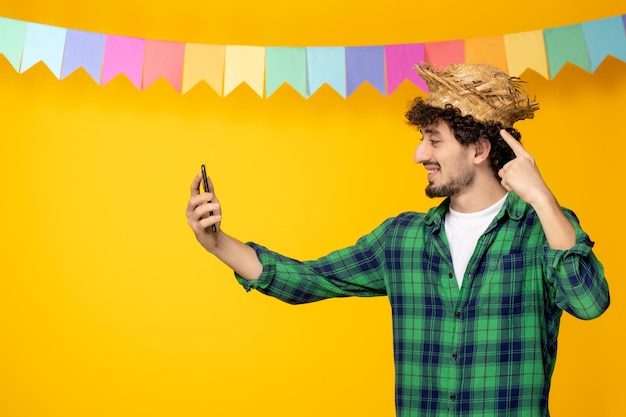 Festa junina jovem bonitinho de chapéu de palha e bandeiras coloridas festival brasileiro tirando uma selfie
