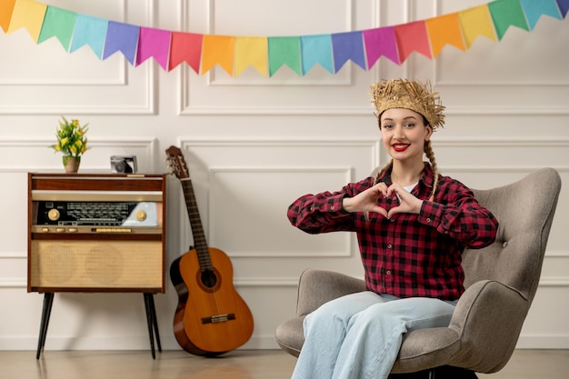 Festa junina linda chica con sombrero de paja verano brasileño con guitarra de radio retro que muestra la mano del corazón