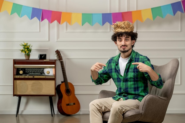 Festa junina lindo joven con sombrero de paja con radio retro y banderas coloridas apuntándose a sí mismo