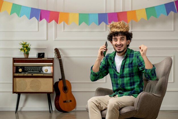 Festa junina lindo joven con sombrero de paja con radio retro y banderas coloridas emocionado en llamada telefónica