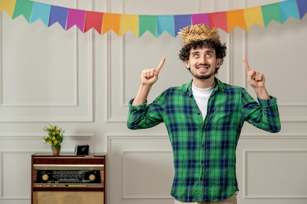 Festa junina lindo joven con sombrero de paja con radio retro y banderas coloridas mirando hacia arriba