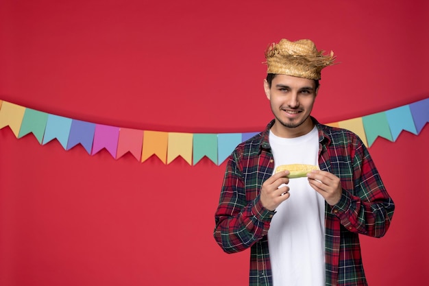 Festa junina sorrindo bonitinho usando chapéu de palha celebrando o festival brasileiro segurando milho