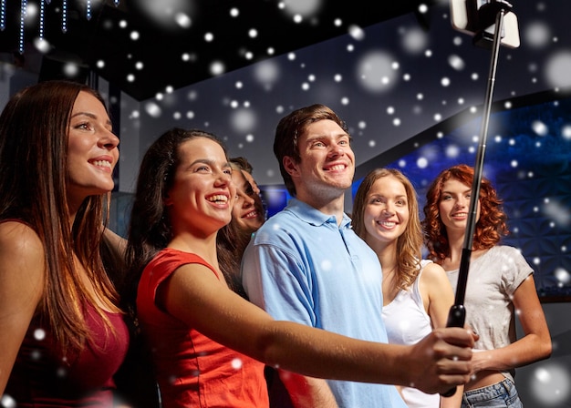 Festa, tecnologia, vida noturna e conceito de pessoas - amigos sorridentes  com smartphone tomando selfie no clube