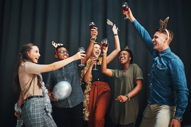 Festejando até o ano novo Foto recortada de um grupo diversificado de amigos em pé e segurando taças de vinho para um brinde no Ano Novo