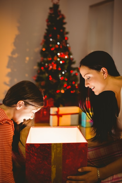 Festiva mãe e filha que abrem um presente brilhante de Natal