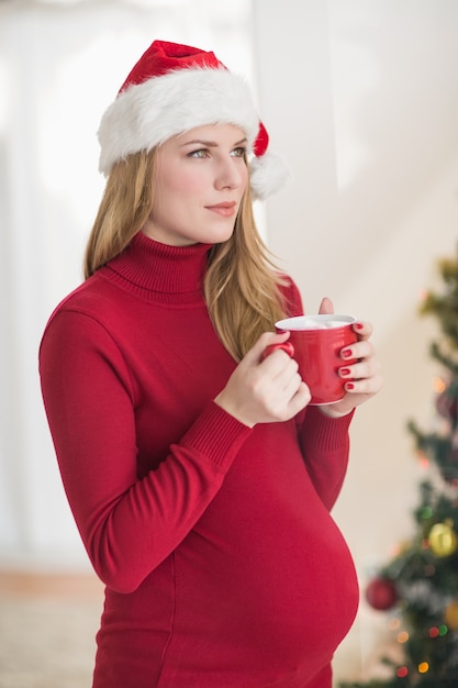 Festiva mujer embarazada sosteniendo la taza mientras está de pie