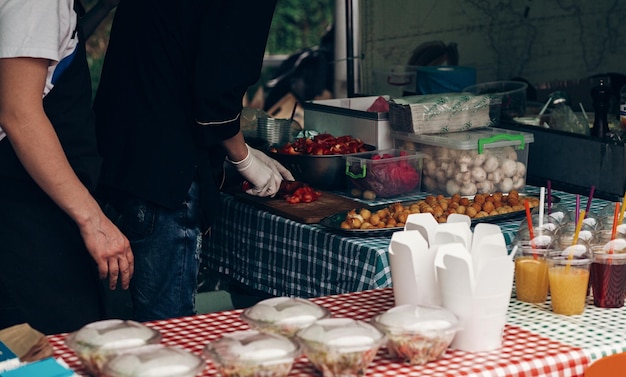 Festival de comida callejera hombre cortando tomate cocinando comida rápida para llevar chef en forma y guantes haciendo ensaladas y barbacoa cocina abierta al aire libre catering picnic de verano