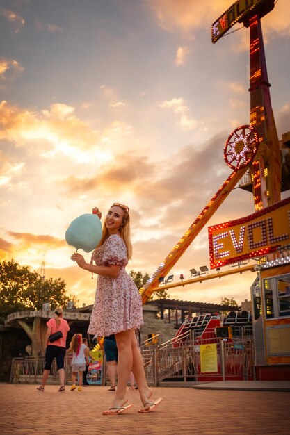 Festival de verão bonita mulher caucasiana em vestido segurando um algodão doce e lazer no parque de diversões