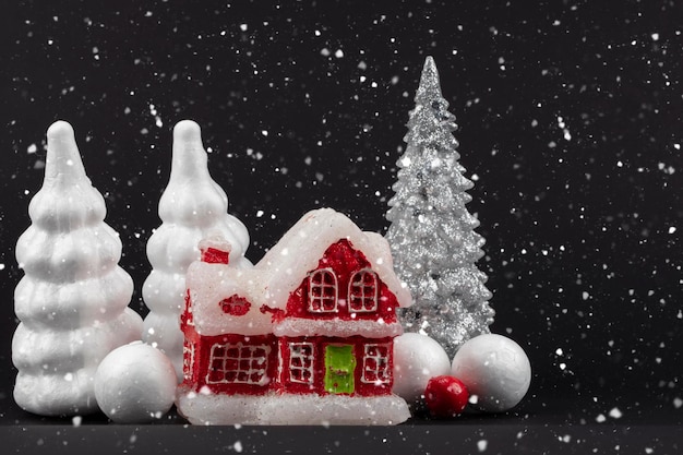 Festivo fundo de Natal escuro e nevado Casa em miniatura vermelha cercada por árvores de Natal brancas