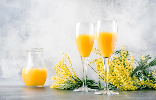 Festliche Alkohol-Cocktail-Mimose mit Orangensaft und kaltem, trockenem Champagner oder Sekt im grauen Barthekenhintergrund der Gläser mit Blumenplatz für selektiven Textfokus