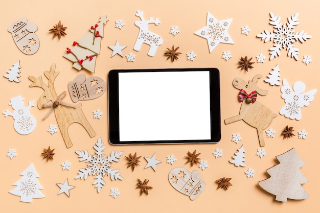 Festliche Dekorationen und Spielzeug auf orangem Hintergrund. Draufsicht des digitalen Tablets. Frohe Weihnachten-Konzept.