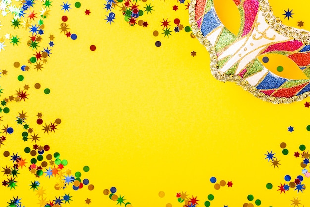 Festliche gelbe Oberfläche mit bunter Karnevalsmaske. Grußkartenkonzept für Geburtstag, Karneval, Party. Kopierraum, Draufsicht, flache Lage
