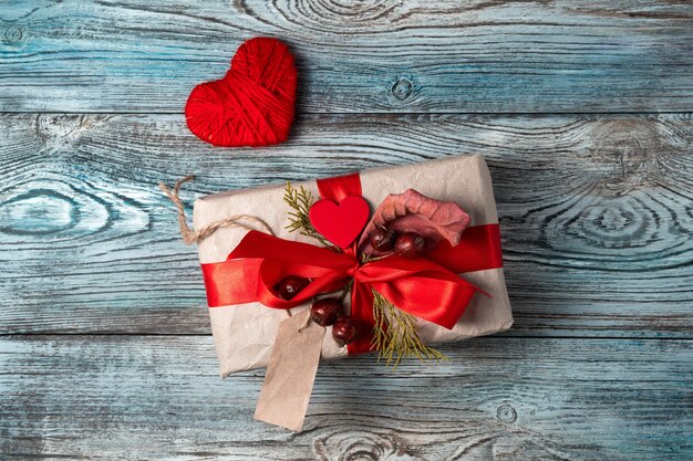 Festliche Komposition mit einem Geschenk und einem Herzen auf einem grau-blauen hölzernen Hintergrund.