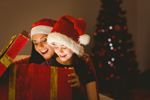 Festliche Mutter und Tochter, die ein Weihnachtsgeschenk öffnen