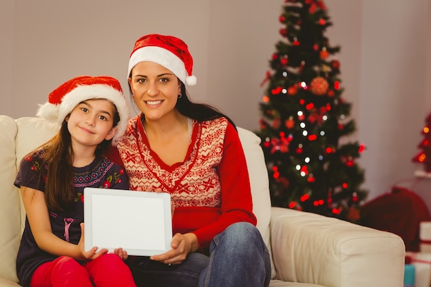 Festliche Mutter und Tochter, die Tablettenschirm zeigt