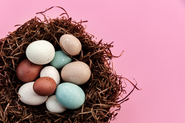 Festliche Ostereier im Nest gegen rosa Hintergrund, traditionelle Dekoration für zu Hause am saisonalen Feiertag