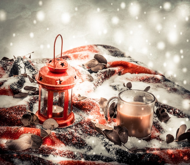 Festliche rote Kerze in Laterne und Tasse Kaffee auf Teppich mit Schnee