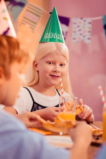 Festliche Stimmung. Positiv entzückte kleine Frau, die in der Mitte des Tisches sitzt, während sie ihren Klassenkameraden ansieht