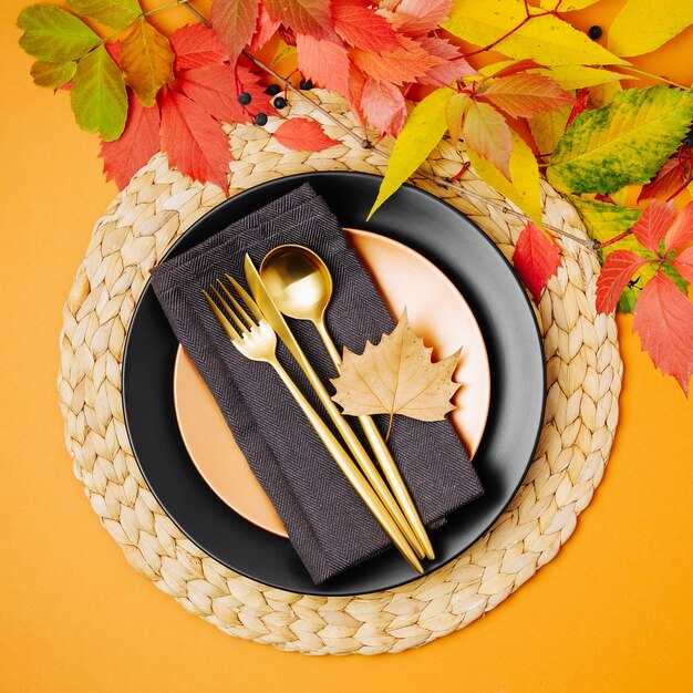 Festliche Tischdekoration mit hellem Herbstlaub auf pastellfarbenem Hintergrund.